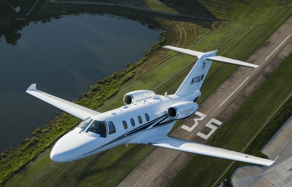 A Cessna Citation M2, powered by Williams FJ44 engines, banking over a runway in flight