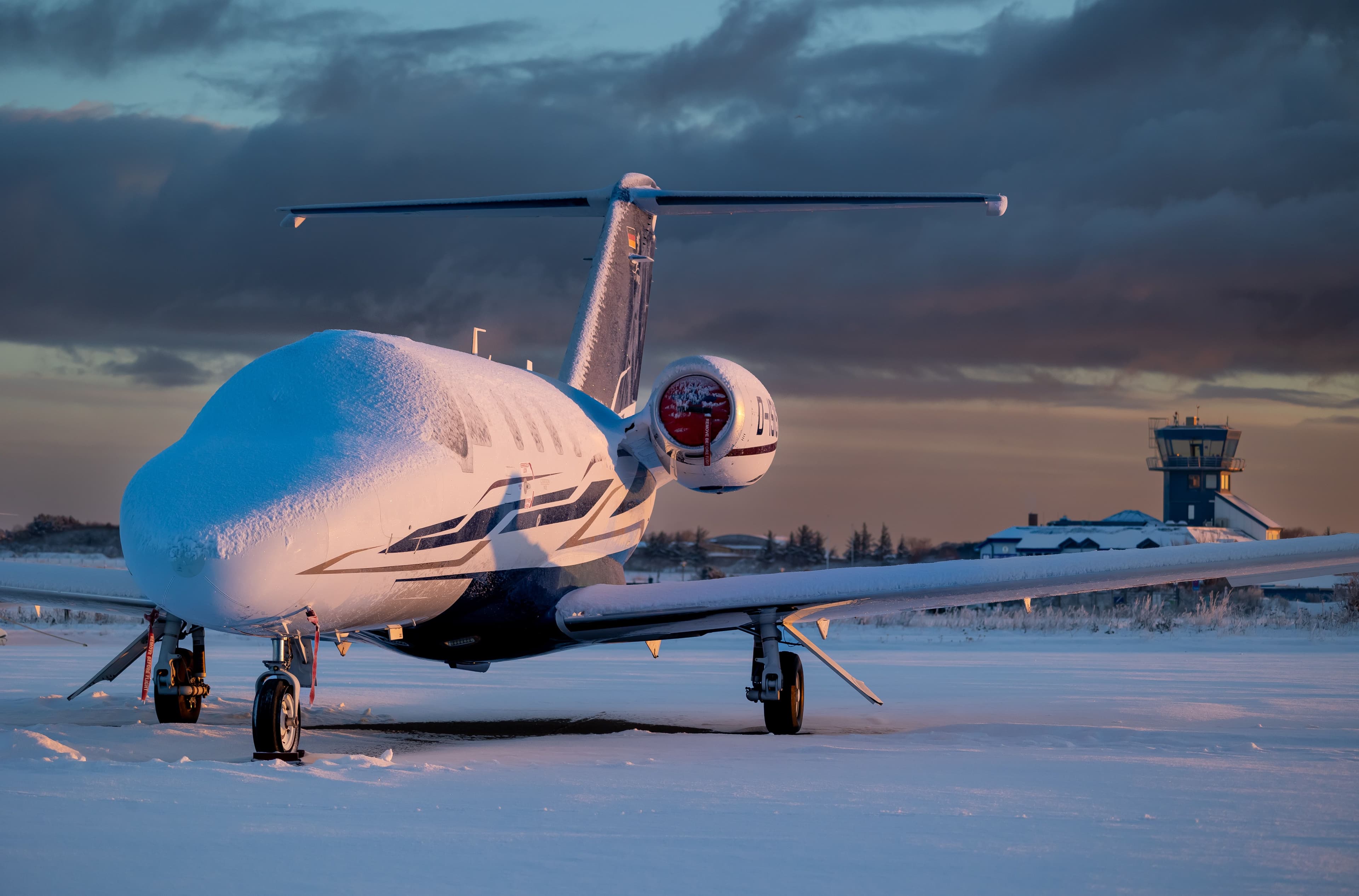 Snow-covered business jet parked on a frozen airport ramp at sunrise, awaiting deicing